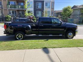 A black 2015 Chevrolet Silverado 3500HD pickup truck with a long bed visible from the side angle showcasing its large wheels and robust build