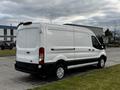 A white 2020 Ford Transit cargo van with a high roof and sliding side door parked on a grassy area