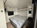 Interior of a 2022 Keystone Hideout RDWE 20RDWE featuring a bed with a mattress and a shelf above it along with a TV mounted on the wall and a large window with blinds