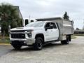 A 2021 Chevrolet Silverado 3500HD white pickup truck with a large gray dump bed on the back and black wheels