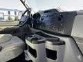 The interior of a 2019 Ford Econoline showing the dashboard with controls and cup holders, including the steering wheel and seat in the foreground