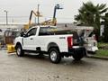 A white 2023 Ford F-250 truck equipped with a snow plow attachment and a salt spreader in the truck bed parked on a street