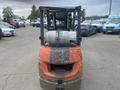 A 2010 Toyota 7FGGU25 forklift facing forward with a propane tank mounted on the mast and a worn red and black exterior