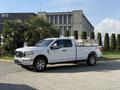 A white 2021 Ford F-150 pickup truck is parked at an angle showing its side and front with chrome wheels and a utility bed setup