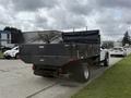 A 2021 Ford F600 truck with a flatbed and a black tarp secured on the cargo area parked on the side of the street