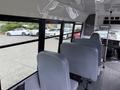 Interior view of a 2013 Chevrolet Express showing grey seats arranged in a row with a dashboard visible in the front and large windows on the sides