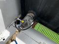 A close-up of a machinery connection featuring a rusty metal fixture with a blue and yellow valve and a green corrugated hose attached to it