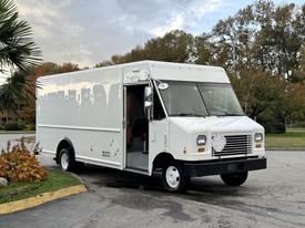 A white 2012 Ford Econoline delivery truck with a boxy design and an open front door displaying a driver seat area