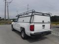 A white 2015 Chevrolet Silverado 1500 with a truck bed cover and roof rack parked on a gravel surface