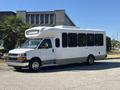 A 2017 Chevrolet Express bus with a white exterior and large windows parked on a gravel surface