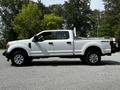 A 2017 Ford F-250 SD pickup truck in white with a crew cab and black rims parked on a gravel surface