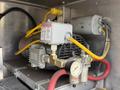 A close-up view of a mechanical component featuring yellow and red hoses connected to a silver pressure gauge and a motor assembly