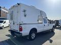 A white 2014 Ford F-350 SD with a camper shell mounted on the bed and a prominent rear tailgate