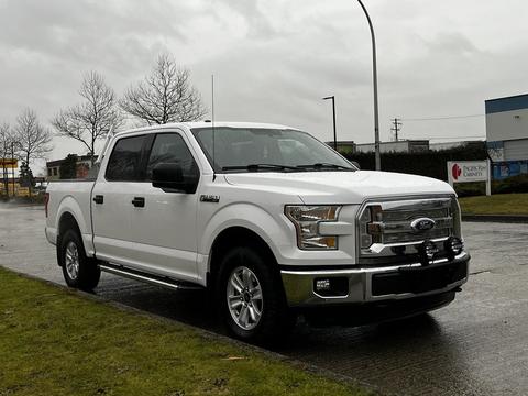 A white 2015 Ford F-150 pickup truck with chrome accents and a crew cab design is parked on a street