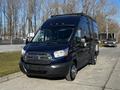 A black 2017 Ford Transit van parked on a street with a roof rack and chrome front grille