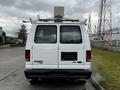 White 2011 Ford Econoline van with a roof rack and equipment mounted on top seen from the rear