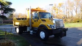 A yellow 2009 International 7400 dump truck with a black front bumper and large wheel wells parked at an angle with its bed raised