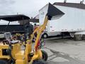 A 2024 AGT Industrial KRW23 Mini Loader with a black bucket and yellow chassis is positioned in the foreground with visible controls and seating area