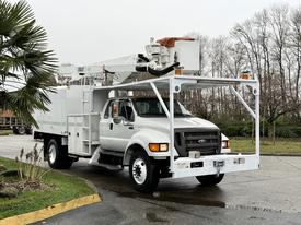 A 2015 Ford F750 with a white body and an extended hydraulic arm attached to the top for lifting and maintenance tasks