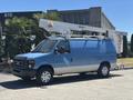 A blue 2008 Ford E-350 van with a white bucket lift attached to its roof parked on a street