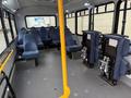 Interior view of a 2017 Chevrolet Express showing rows of blue fabric seats and two operator seats with control panels attached