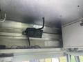 A black audio speaker mounted on a silver metal shelf with visible wiring and labels on the shelf underneath