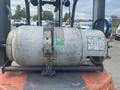 A propane tank secured on a forklift with a warning label and markings visible on its surface