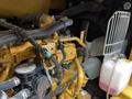 A close-up of a yellow Caterpillar 306 engine showcasing various pipes wires and a fan system along with a coolant reservoir
