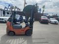 A 2010 Toyota 7FGGU25 forklift with an orange and gray color scheme parked on a lot among various vehicles