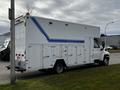 A white 2006 GMC C5000 truck with a large cargo box and multiple side doors, featuring blue stripes along the sides