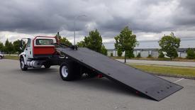 A 2015 International DuraStar 4300 flatbed truck with a tilted loading ramp in a parking area