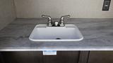 A stainless steel double faucet above a white sink set into a marble countertop