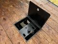 A rectangular opening in a wooden truck bed revealing a black mechanism with a circular knob at the center
