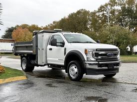 A 2021 Ford F-550 with a flatbed and side storage compartment parked on a wet surface