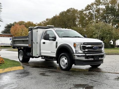 A 2021 Ford F-550 with a flatbed and side storage compartment parked on a wet surface