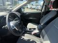Interior view of a 2014 Ford Escape showing the steering wheel and front seats with a light gray fabric and a central console with cup holders and controls
