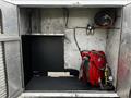 A compartment of a 2006 GMC C5000 featuring a red hose reel with hose and a control panel with two pressure regulators mounted on the wall