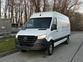 A 2019 Mercedes-Benz Sprinter van in white with a black front grille and headlights parked on a road with trees visible in the background