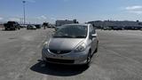 A silver 2006 Honda Fit parked in an open lot with a clear sky in the background