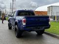 A blue 2022 Toyota Tacoma with a black bed liner and off-road tires parked with its tailgate visible and the model name displayed on the rear