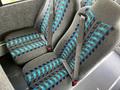 Two gray bus seats with blue and black patterned fabric and safety belts are positioned next to each other in a vehicle interior