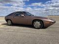 A 1983 Porsche 928 in a copper color with a sleek design and circular alloy wheels