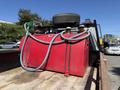A red fuel tank with hoses sits on a truck bed, topped with a spare tire and connected to other equipment