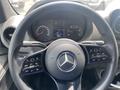 Steering wheel of a 2022 Mercedes-Benz Sprinter with controls for volume and settings visible on the spokes and a digital display on the dashboard in the background