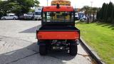 A 2018 Kubota RTV X1100C vehicle with an orange cab and black bed parked on a driveway showcasing its rear view and large tires