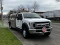 A 2018 Ford F-550 with a silver fuel tank in the bed and a hazard sign on the front bumper parked on a street