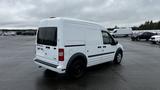 A white 2012 Ford Transit van with a high roof and dual rear doors parked on a wet surface without any visible cargo