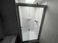 A transparent glass shower enclosure with a modern design featuring a herringbone tile pattern inside and a showerhead attached to the wall