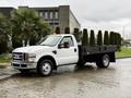 A white 2008 Ford F-350 flatbed truck with a black flatbed and orange roof lights parked on a wet surface