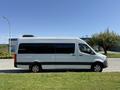 A 2023 Mercedes-Benz Sprinter van in white with black trim parked on grass showcasing its side profile and large windows